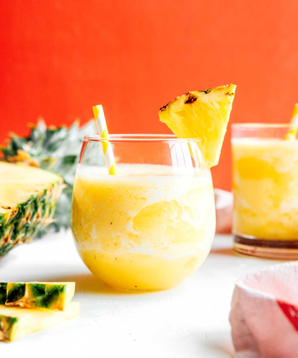 A glass filled with pineapple smoothie and decorated with a slice of pineapple