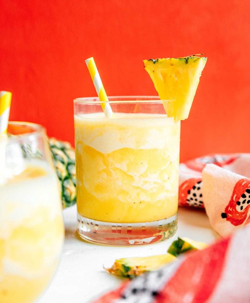 A glass filled with pineapple smoothie and decorated with a slice of pineapple