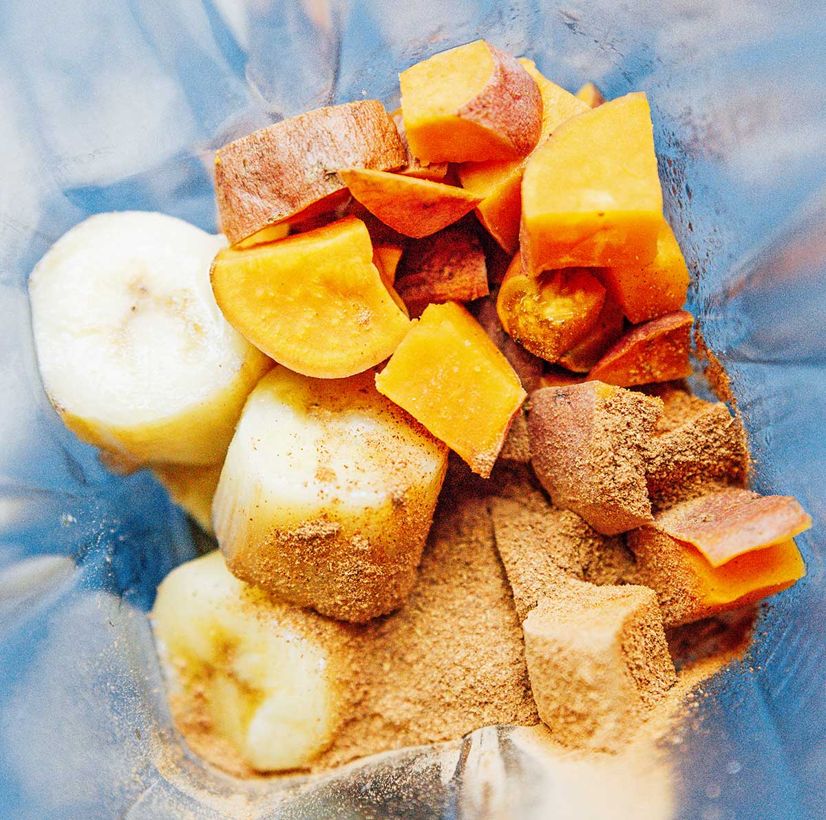 A blender filled with frozen banana chunks, diced sweet potato, and spices 