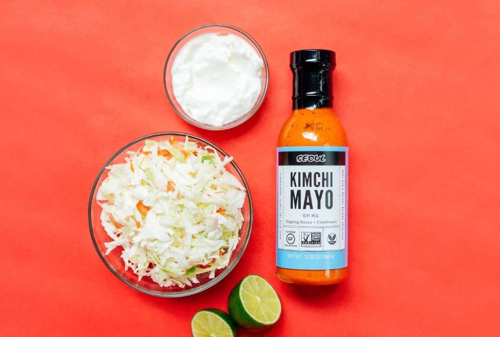 Ingredients to make kimchi mayo slaw in a glass bowl on a red background