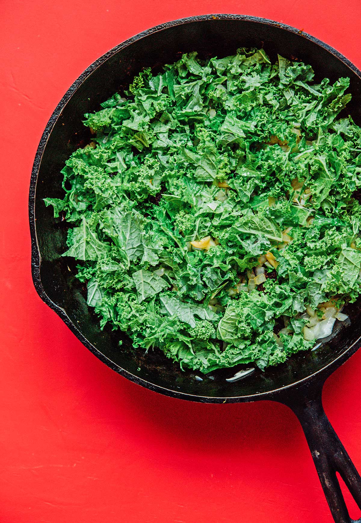 A bed of chopped kale and diced white onion in a cast iron skillet