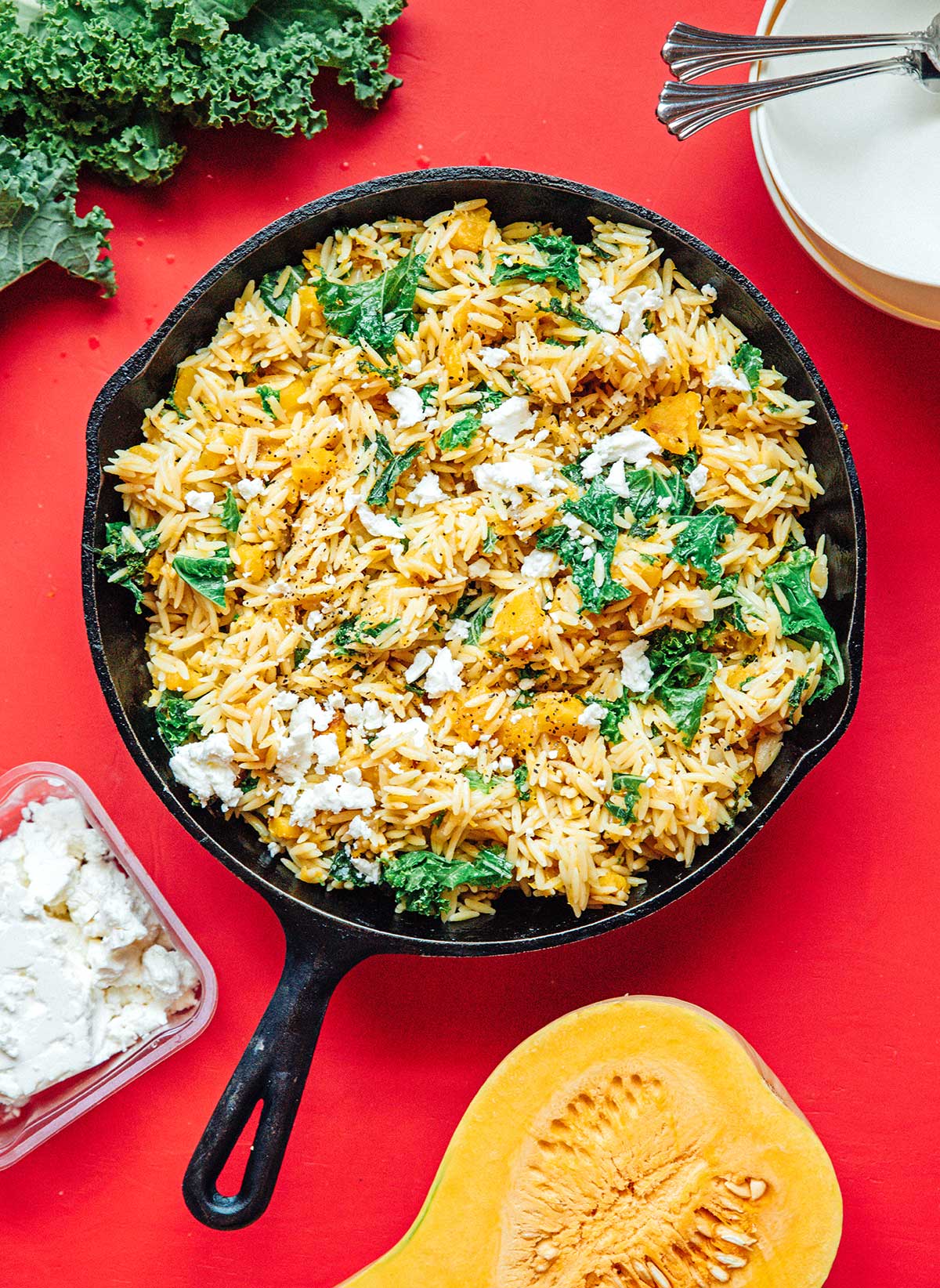 A cast iron skillet filled with cooked kale and white onion, butternut squash, orzo, and various spices