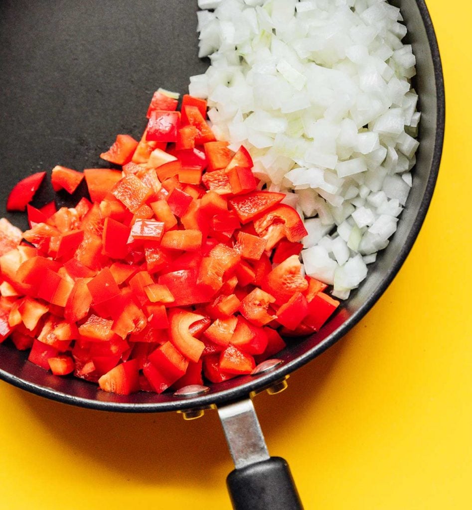 Chopped white onion and red bell pepper in a sauté pan