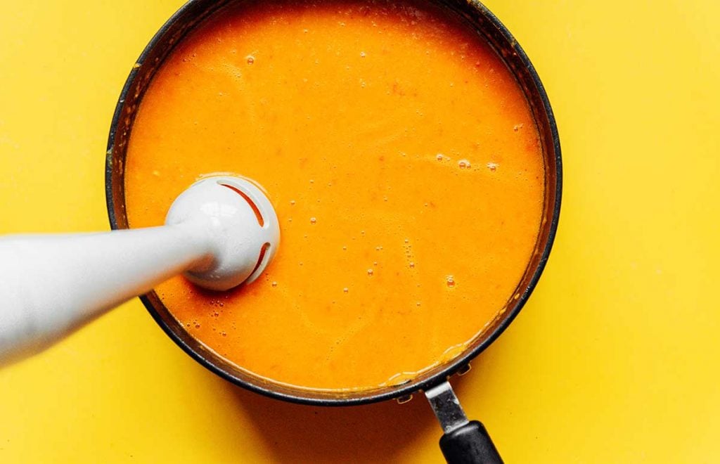 Using an immersion blender to mix together the ingredients in curried butternut squash soup