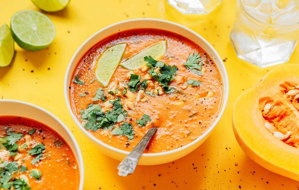 A bowl of curried butternut squash soup topped with fresh cilantro, cashews, and slices of lime