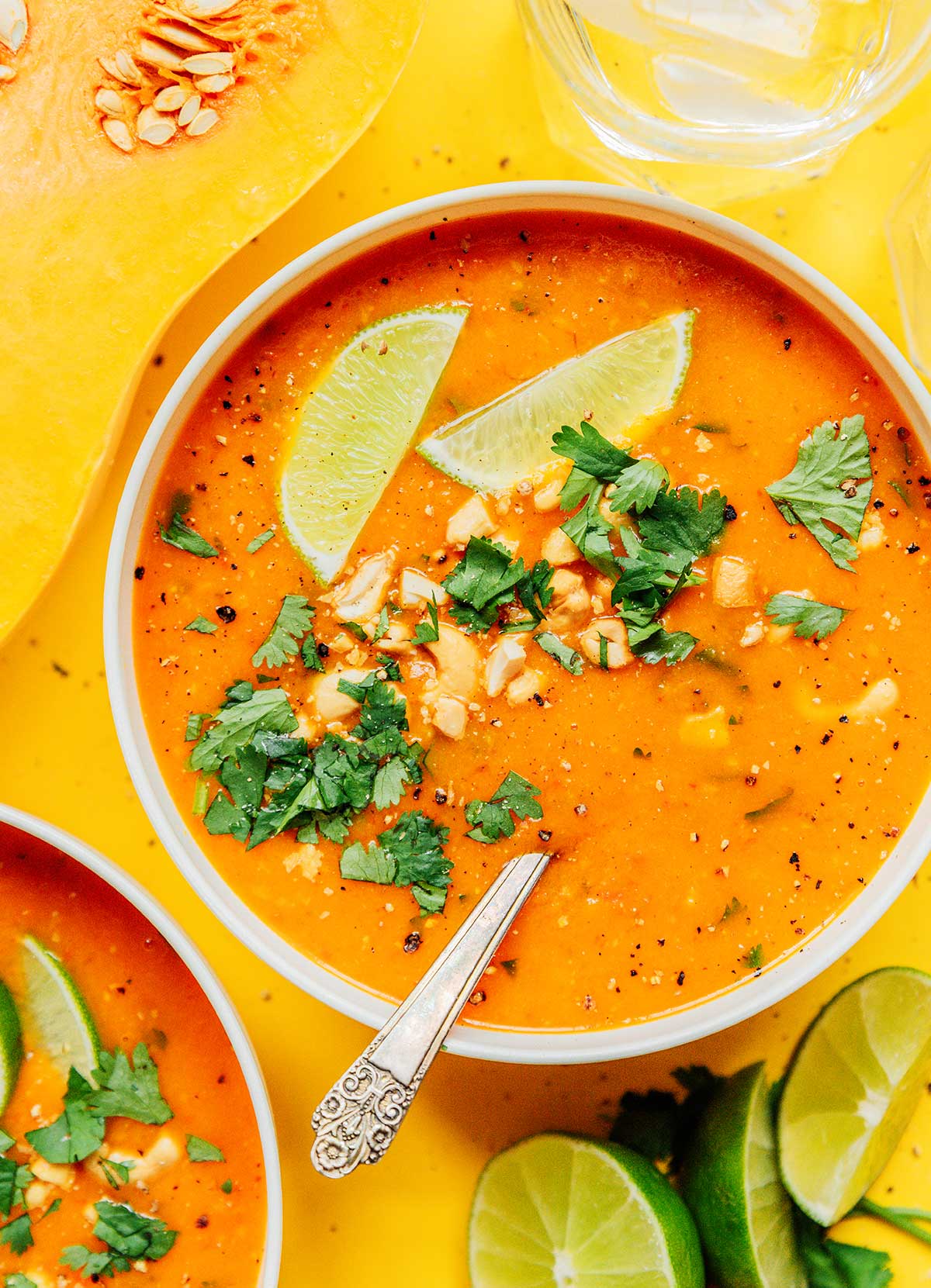 A bowl of curried butternut squash soup topped with fresh cilantro, cashews, and slices of lime