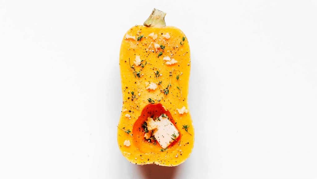 Half of a butternut squash coated with butter, garlic, thyme, and black pepper