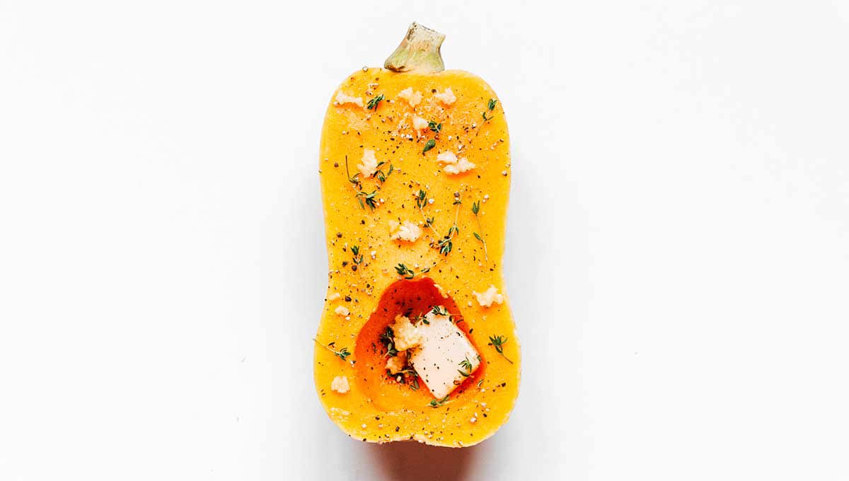 Half of a butternut squash coated with butter, garlic, thyme, and black pepper