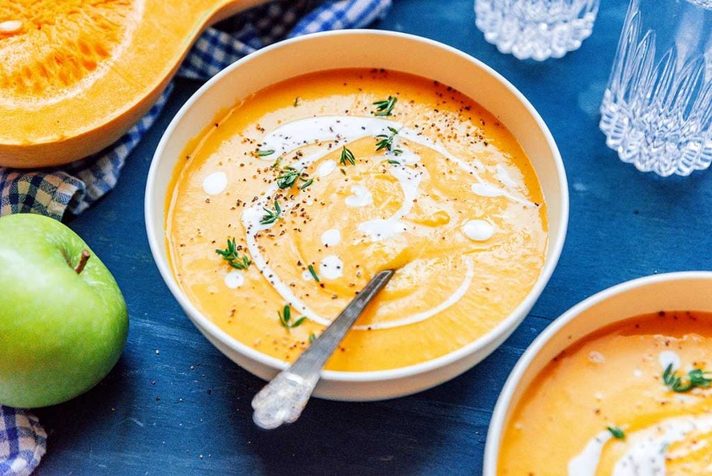 A bowl of vegan butternut squash soup with coconut milk and thyme drizzled and sprinkled on top