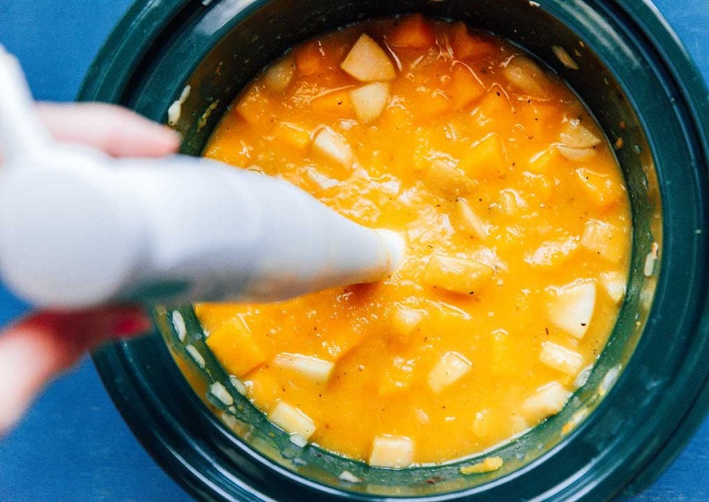 Using a handheld immersion blender to blend the soup ingredients directly inside the slow cooker