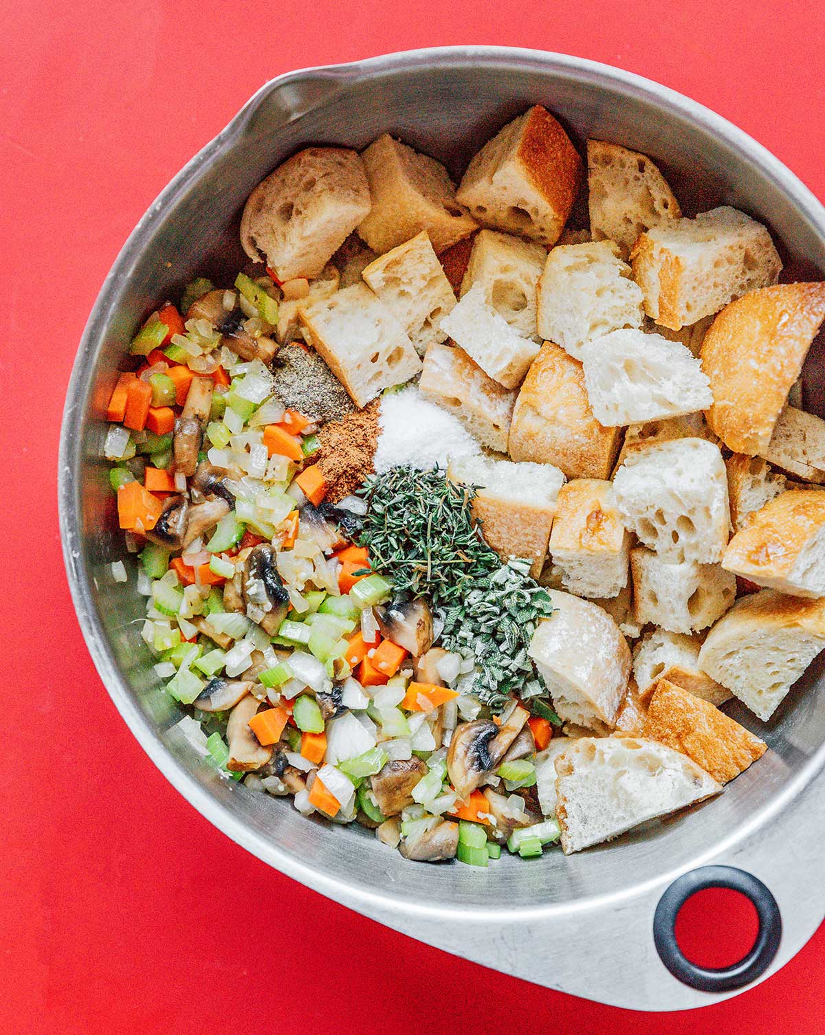 A mixing bowl filled with vegetable bread stuffing ingredients and seasonings 