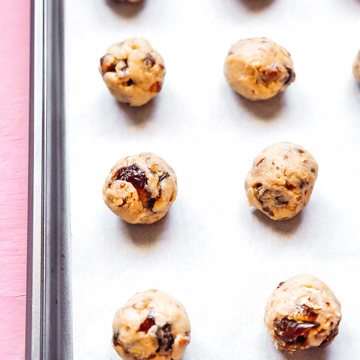Rolled balls of chewy date cookies on a parchment-lined baking sheet ready to go in the oven