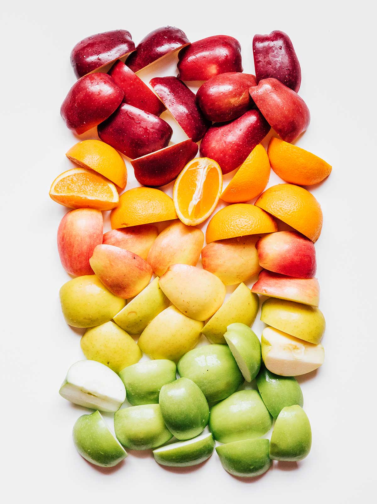 A rainbow of quartered apples and sliced oranges laid out on a white background