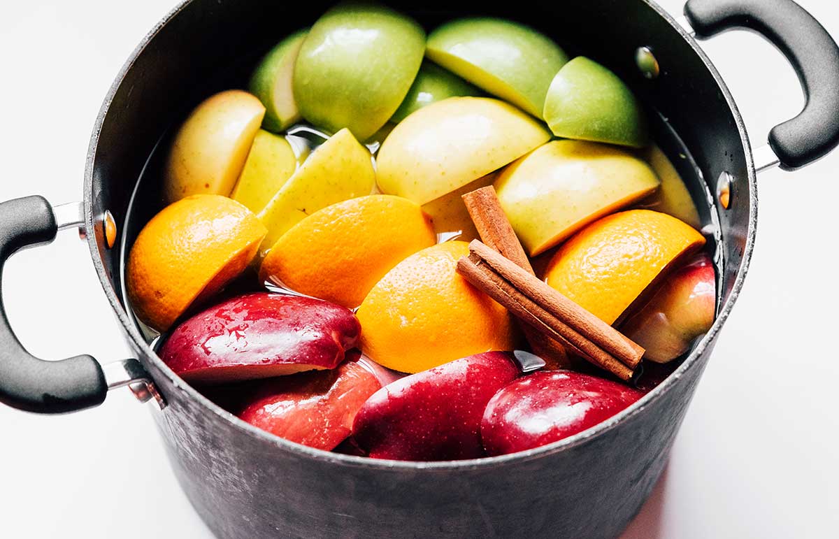 A stove pot filled with homemade apple cider ingredients like quartered apples, sliced oranges and cinnamon sticks