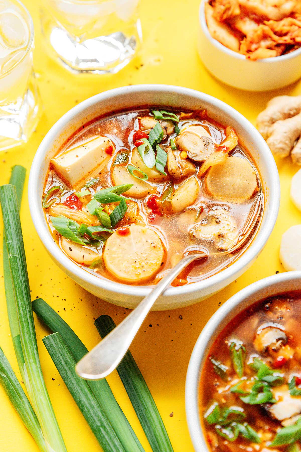 Kimchi soup in a bowl with a spoon on a yellow background