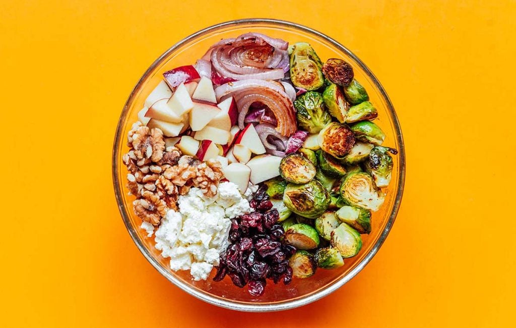 A clear glass bowl filled with all of the roasted Brussels sprout salad ingredients