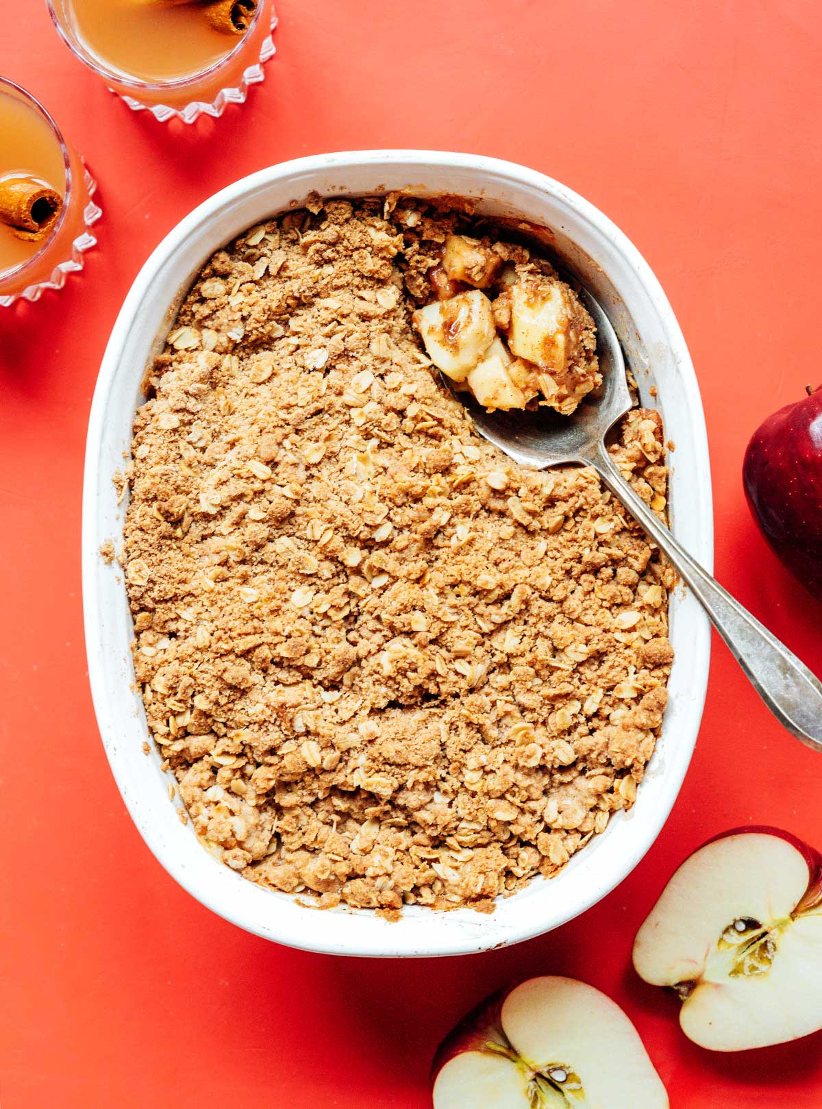 A metal spoon scooping a spoonful of vegan apple crisp from a casserole dish 