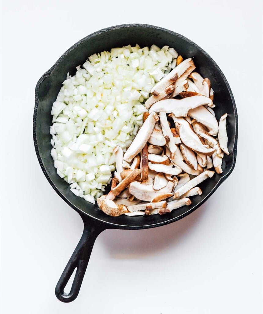 A cast iron skillet filled with chopped onion and sliced mushrooms