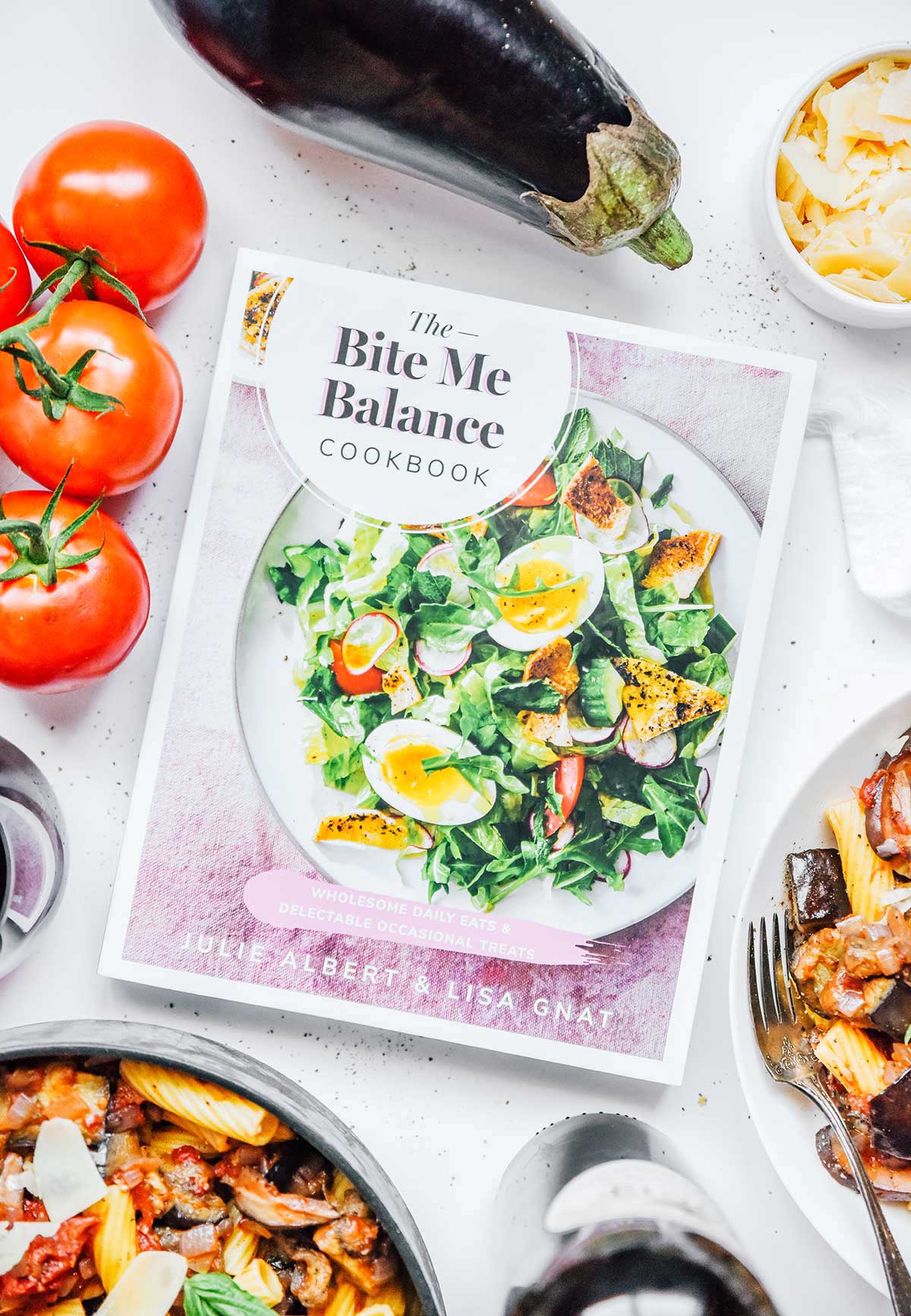 "The Bite Me Balance Cookbook" surrounded by dishes of vegetable bolognese and various ingredients