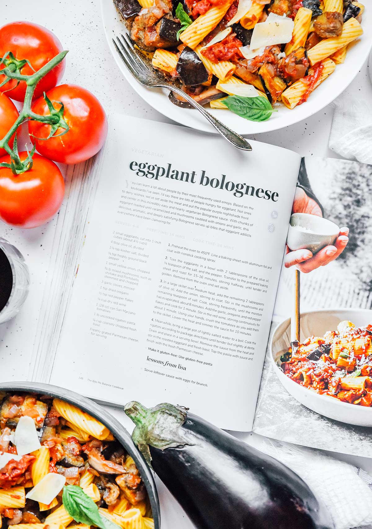 "The Bite Me Balance Cookbook" opened to the Eggplant Bolognese page, surrounded by the completed dish and a few tomatoes