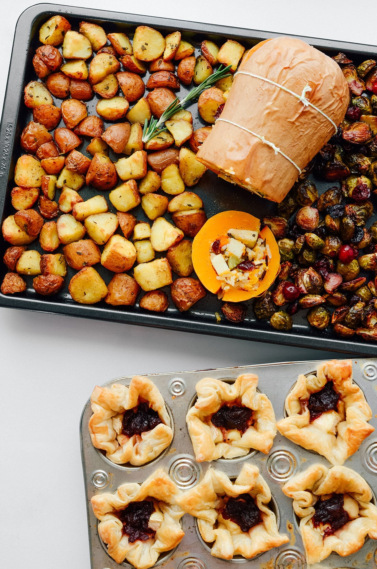 Stuffed butternut squash vegetarian Thanksgiving main dish with crispy potatoes and Brussels sprouts on a baking sheet