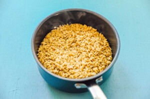 A saucepan filled with cooked bulgur wheat sits on a light blue surface, reminiscent of the texture found in a fresh freekeh salad.