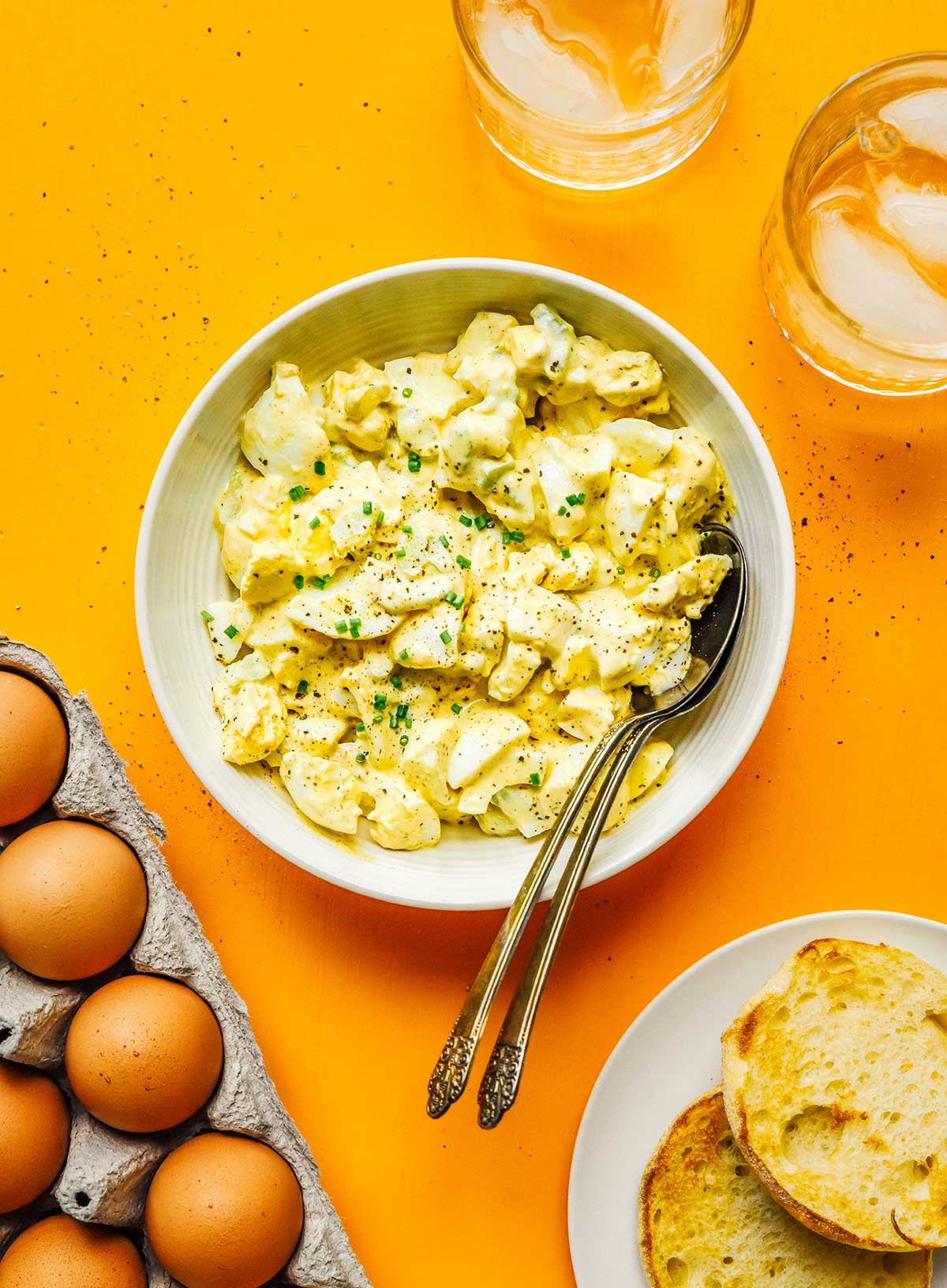 A white ceramic bowl filled with fresh healthy egg salad with two spoons dipped in