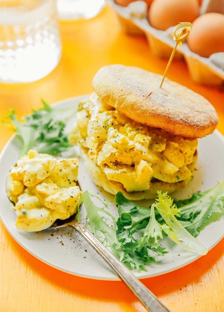 A plate filled with an egg salad sandwich and a side of greens