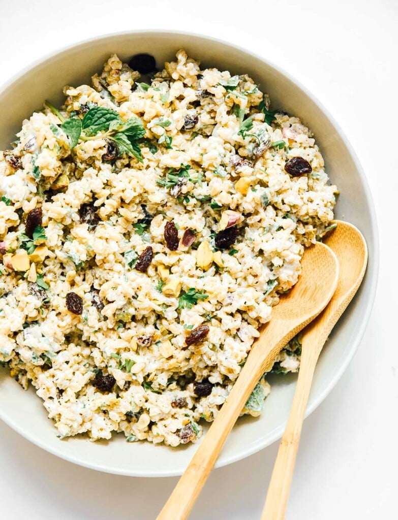 A white bowl filled with freekeh salad, consisting of freekeh, cranberries, corn, basil, and more