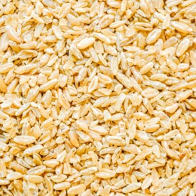 Close-up view of a pile of uncooked, dry grains, possibly barley or wheat, with a yellowish hue—a perfect starting point for learning how to cook freekeh.