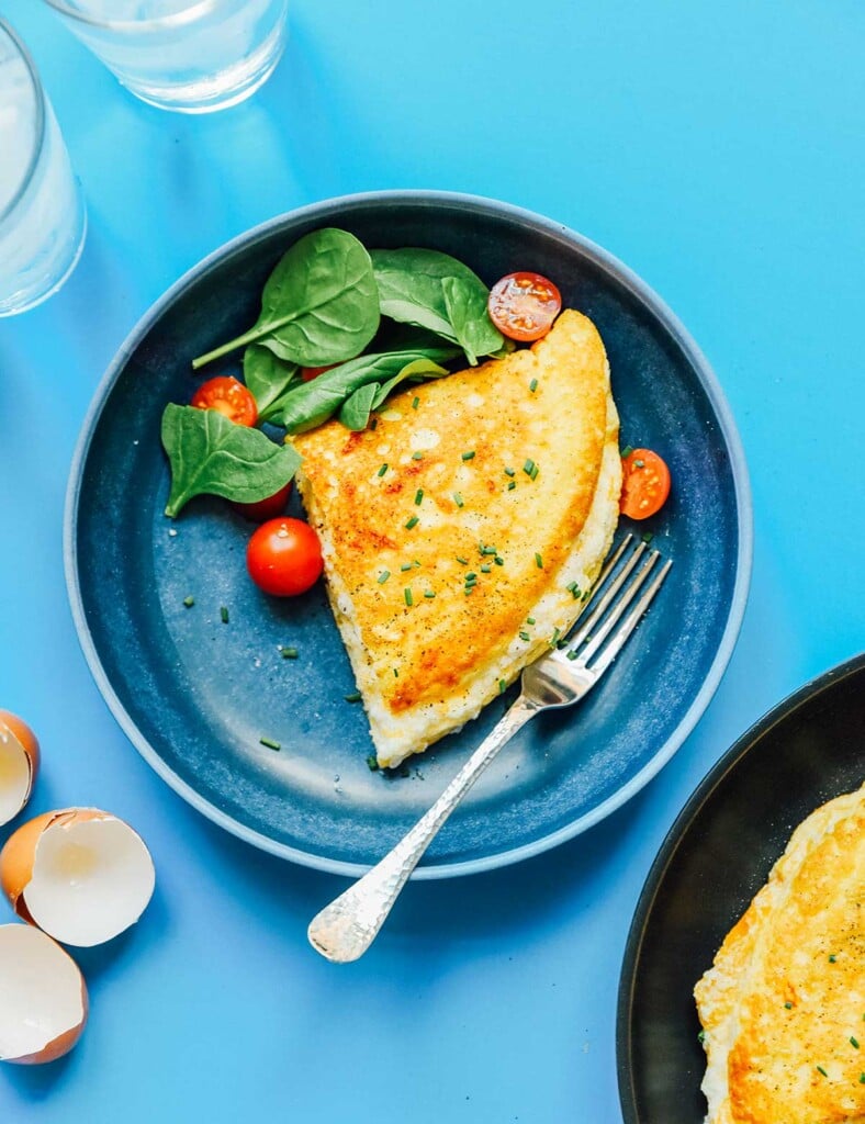 Half of a folded fluffy soufflé omelette on a plate alongside spinach and cherry tomatoes
