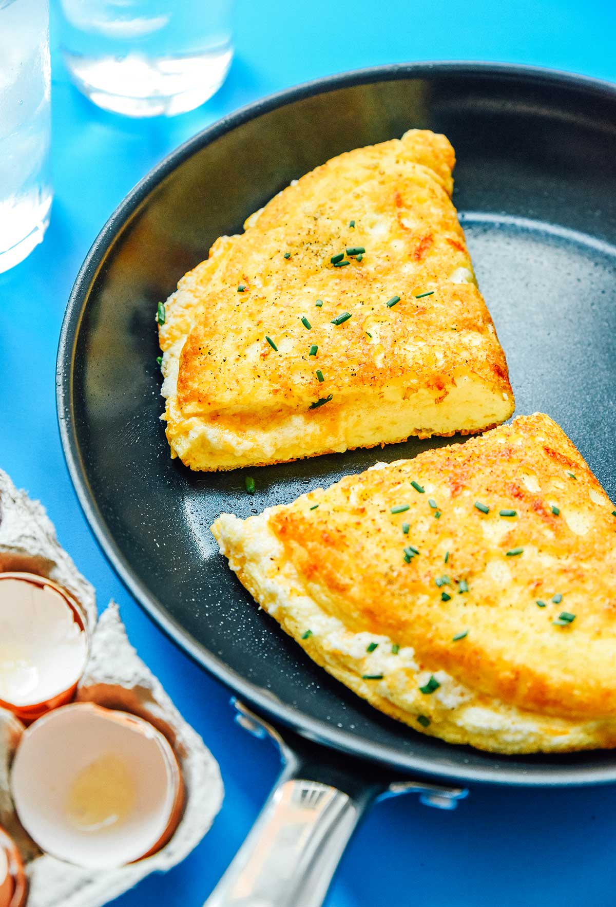 Two halves of a folded, fluffy soufflé omelette in a skillet