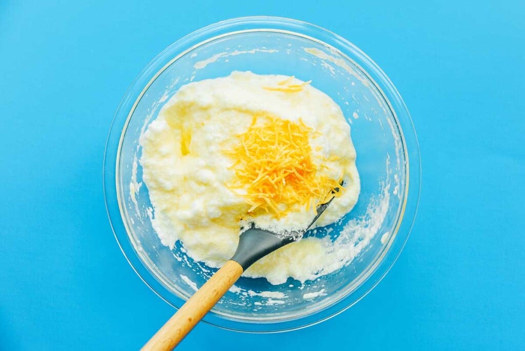A clear bowl filled with mixed egg yolks and whites and topped with shredded cheddar cheese