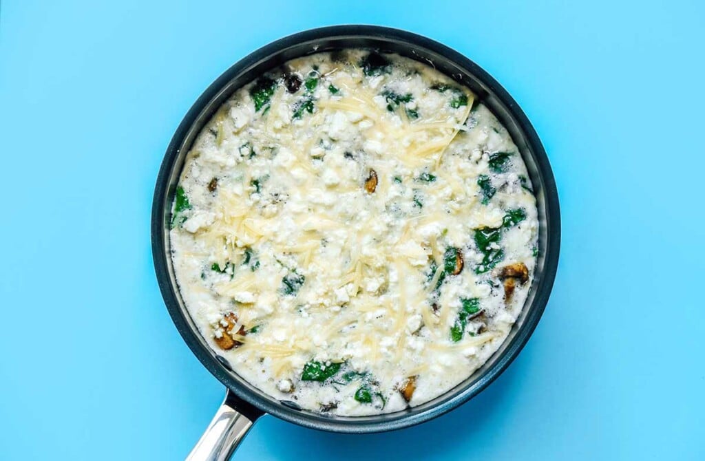 A skillet filled with sautéed mushrooms and spinach with the egg white mixture poured on top