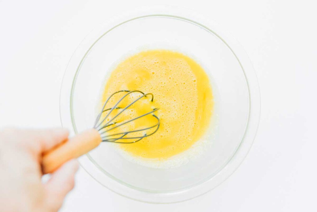 Whisking egg yolks and whole eggs in a clear glass bowl