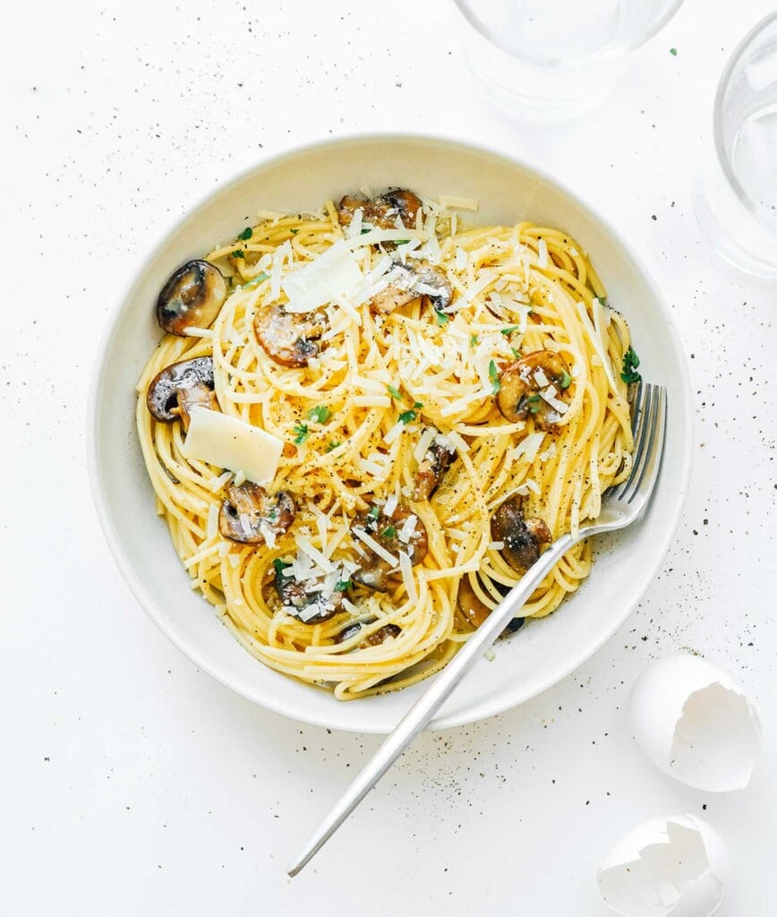 A white bowl filled with vegetarian carbonara and topped with butter, parmesan, and parsley. 
