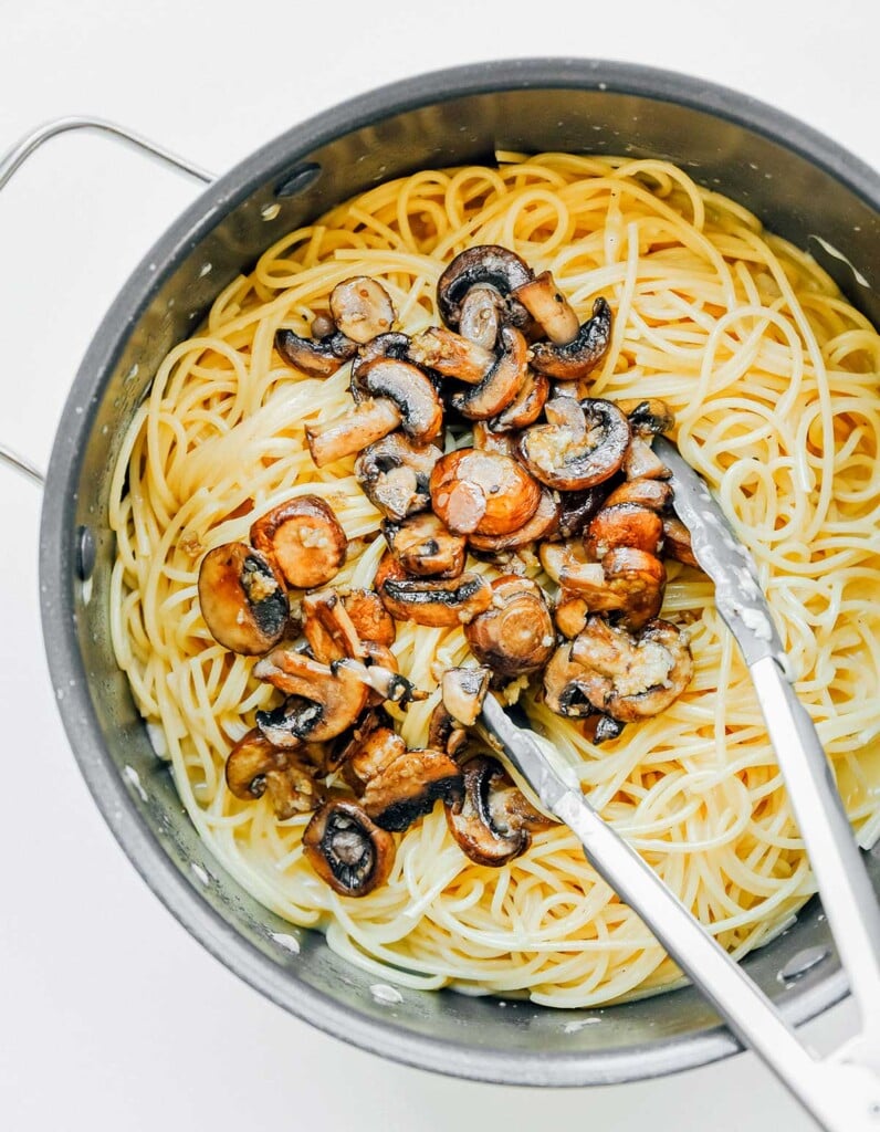 Cooked spaghetti noodles and sautéed mushrooms in a large pot 