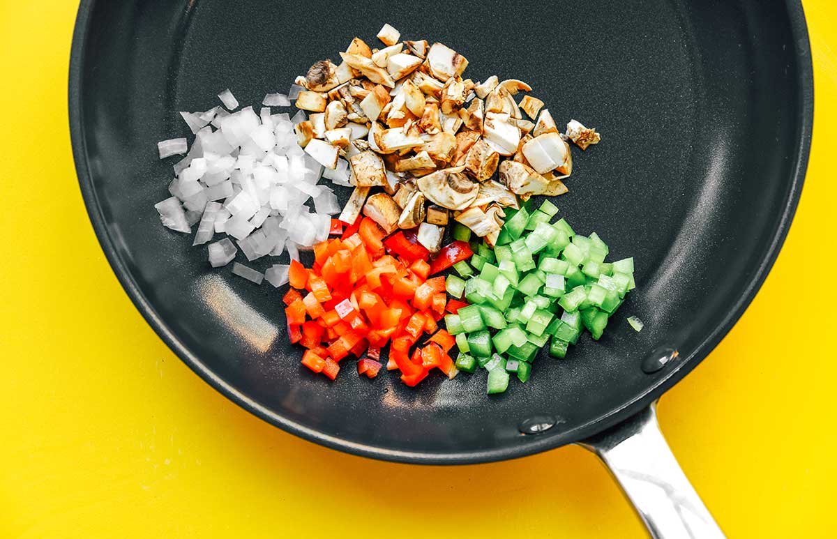 A skillet filled with chopped mushroom, onion, red bell pepper, and green bell pepper