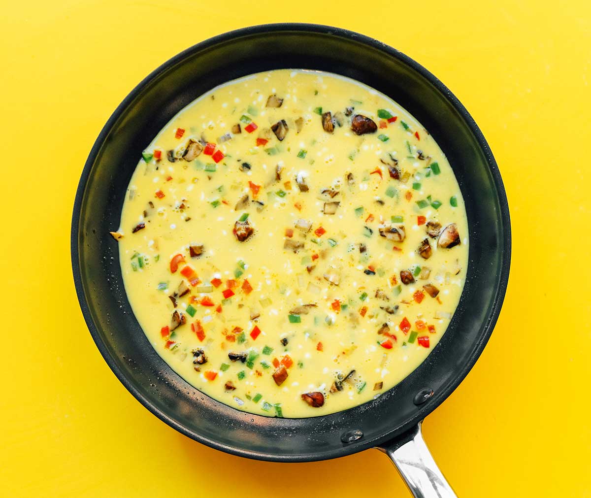 A skillet filled with uncooked omelette ingredients