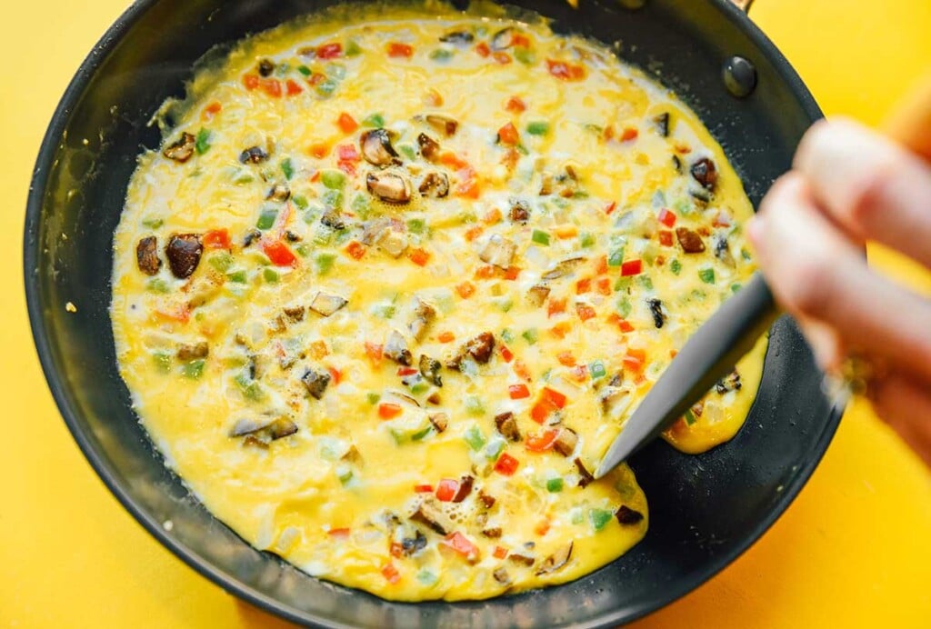 Pushing an omelette edge away from the side of a skillet with a wooden spatula 
