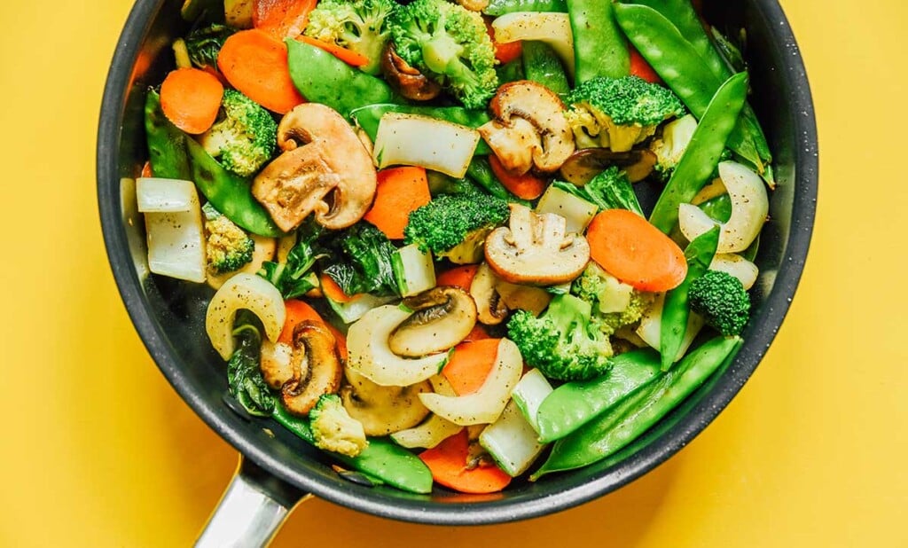 A skillet filled with freshly cooked carrots, snow peas, broccoli florets, bok choy, and mushrooms