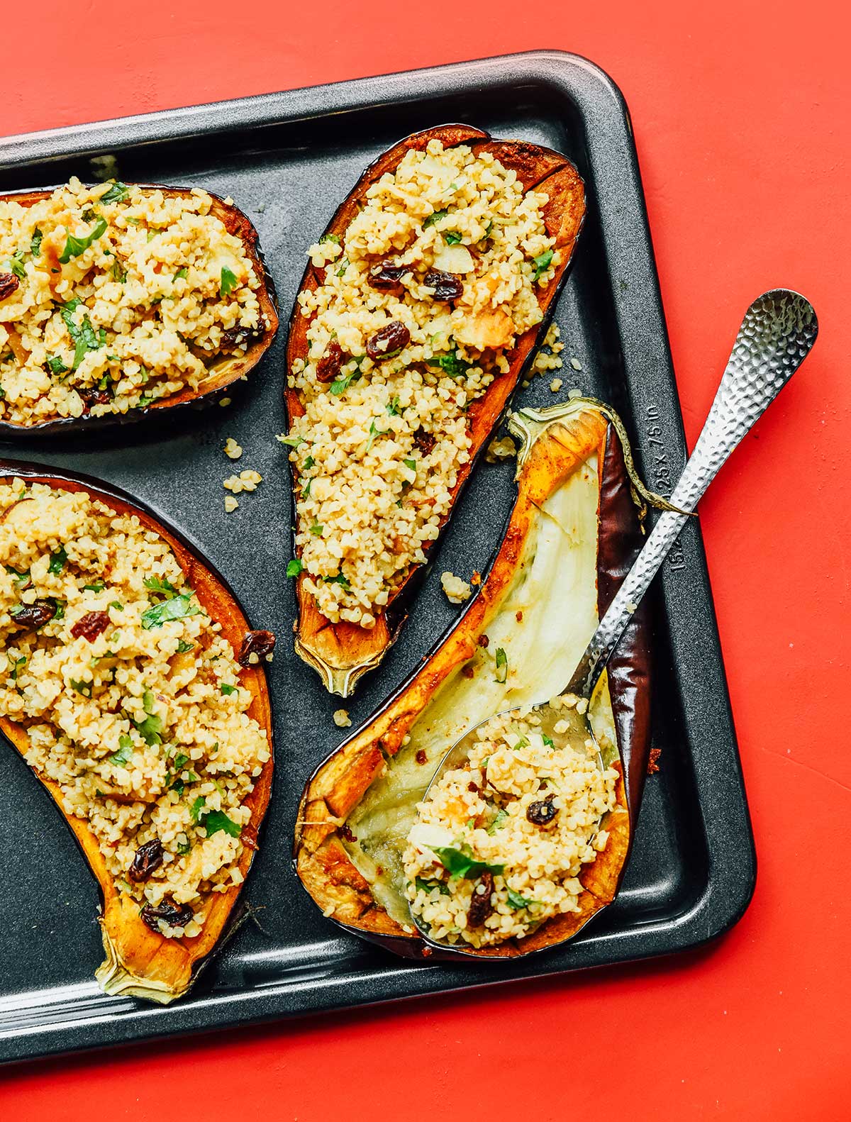 A baking sheet with three stuffed eggplants and a fourth that is begin filled with the stuffing