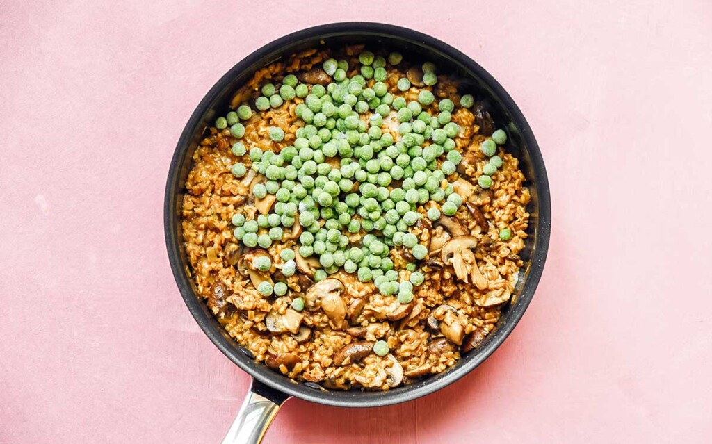 A skillet filled with cooked farro risotto ingredients with frozen peas on top