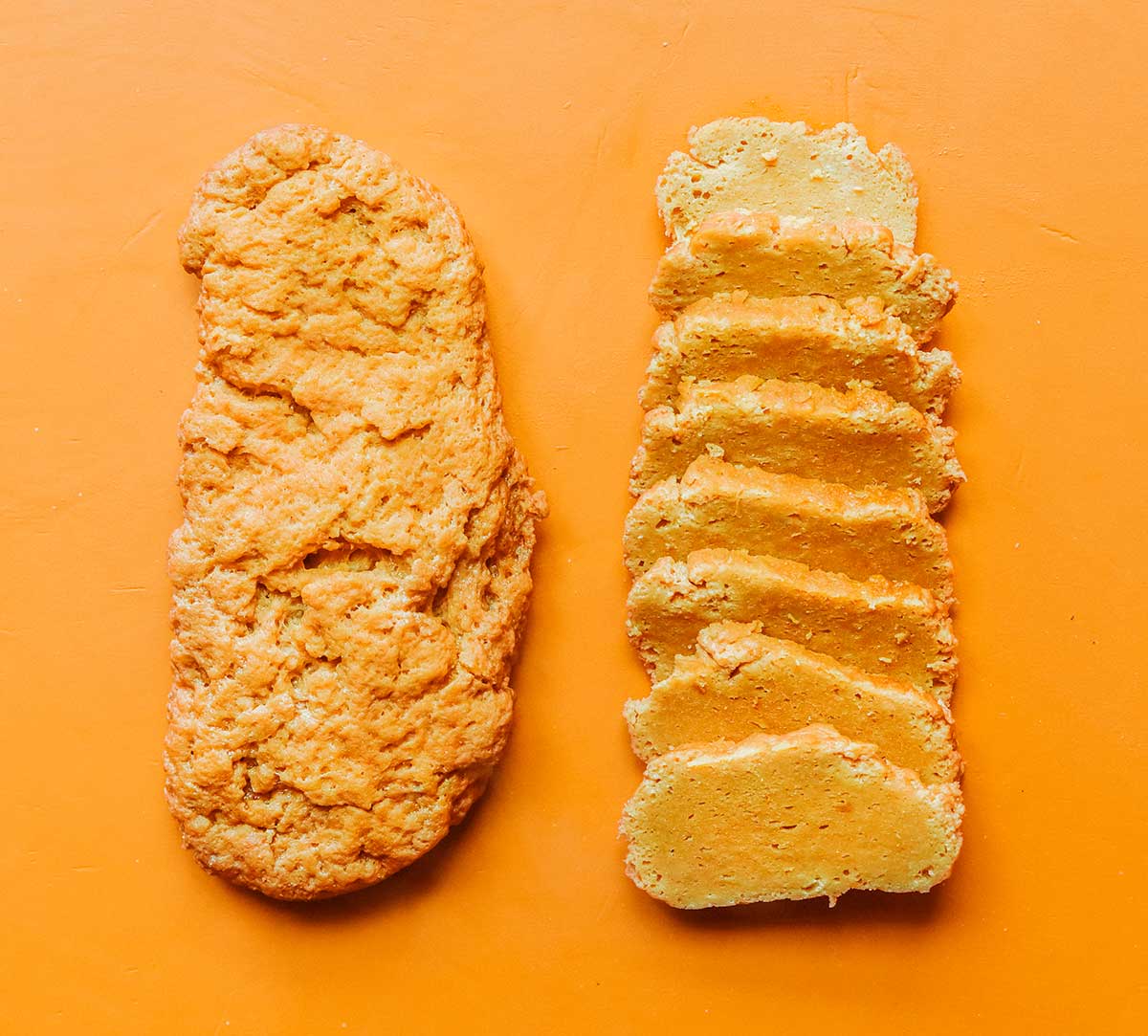 A whole and a sliced loaf of seitan sitting side by side on an orange background