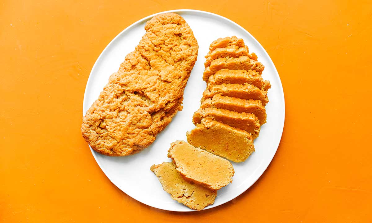 A whole and a sliced loaf of seitan sitting side by side on a white plate