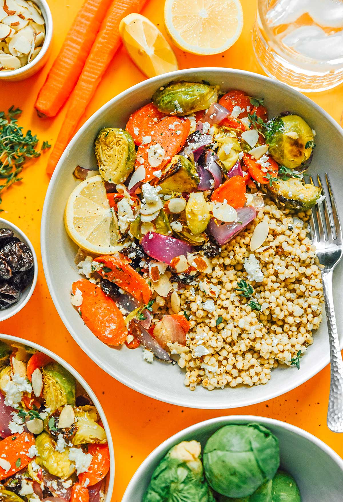 A roasted vegetable grain bowl filled with seitan, red onion, Brussels sprouts, carrots, lemon slices, feta cheese, and more