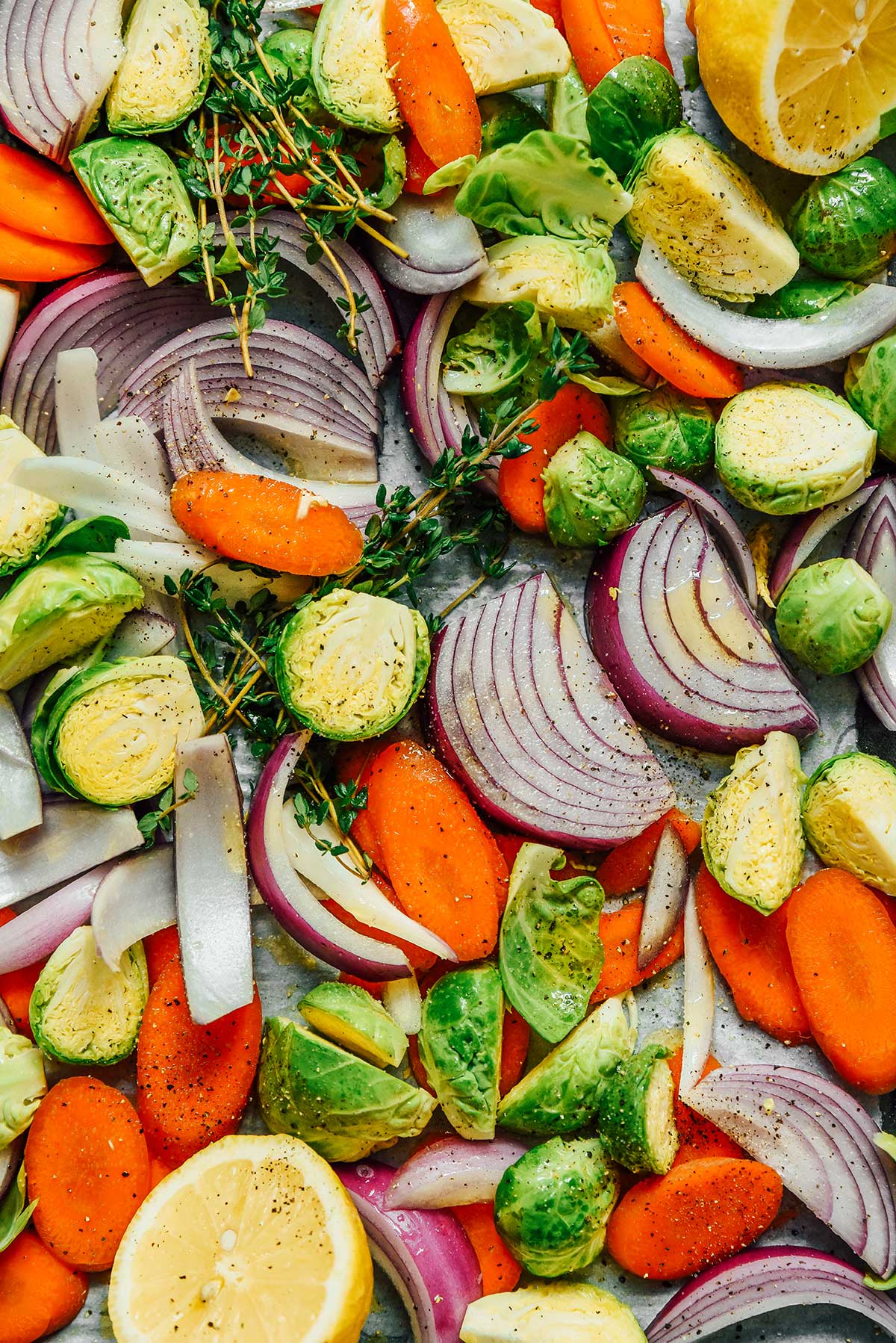 A close-up view detailing the texture of freshly seasoned red onion slices, carrot slices, and halved Brussels sprouts