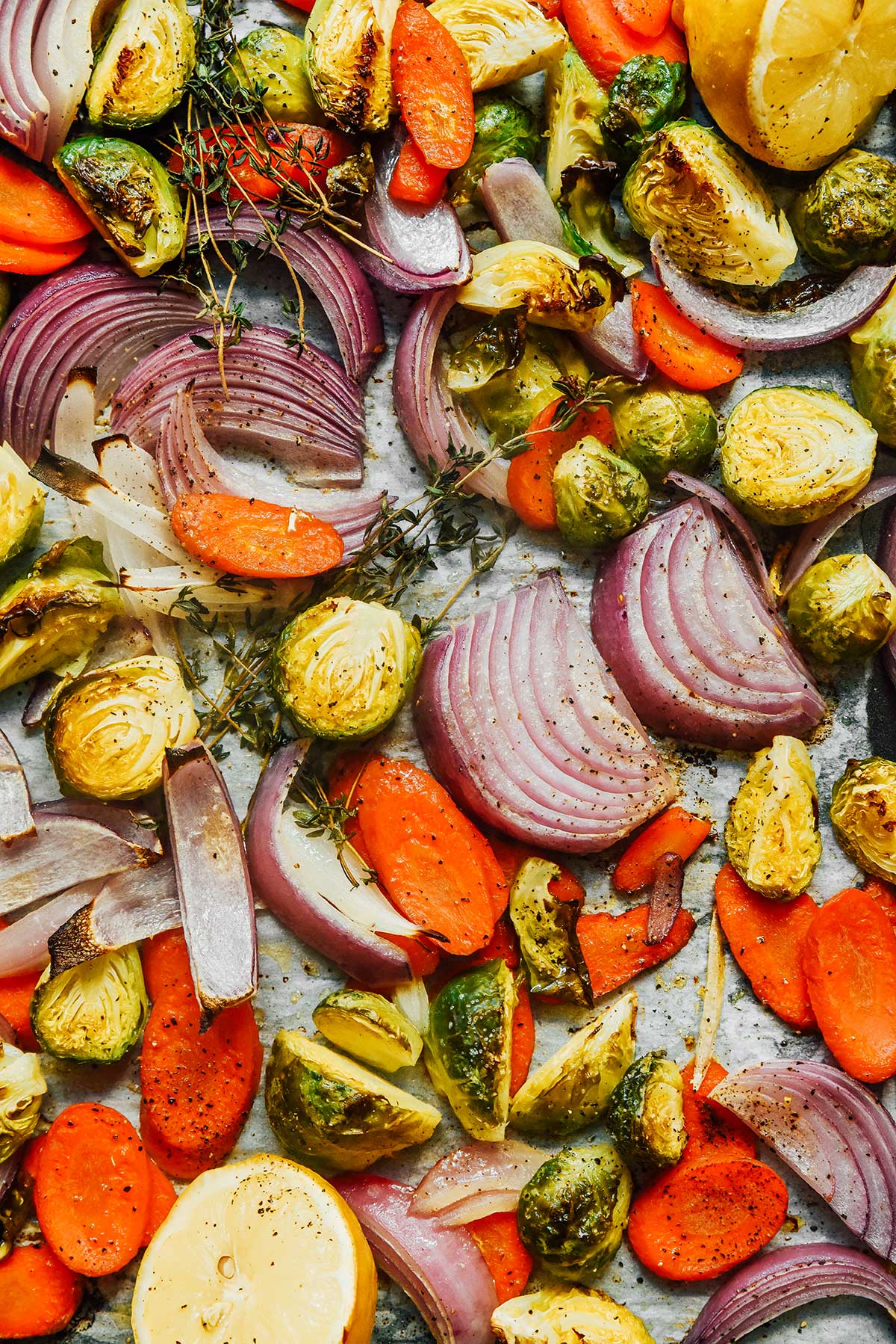A close-up view detailing the texture of freshly roasted red onion slices, carrot slices, and halved Brussels sprouts