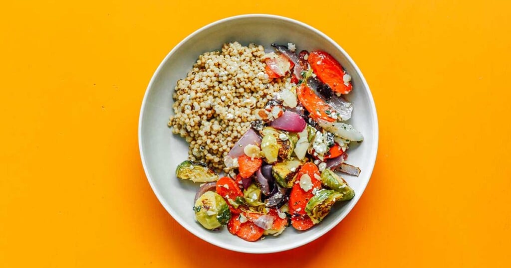 A white bowl filled with roasted vegetable grain bowl ingredients 