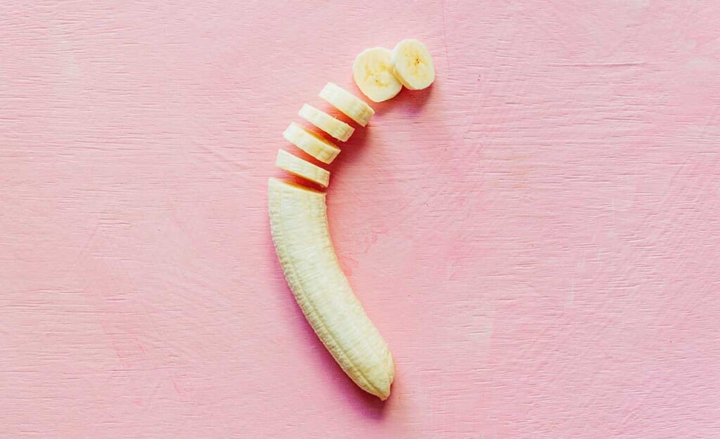 A partially sliced banana on a pink background